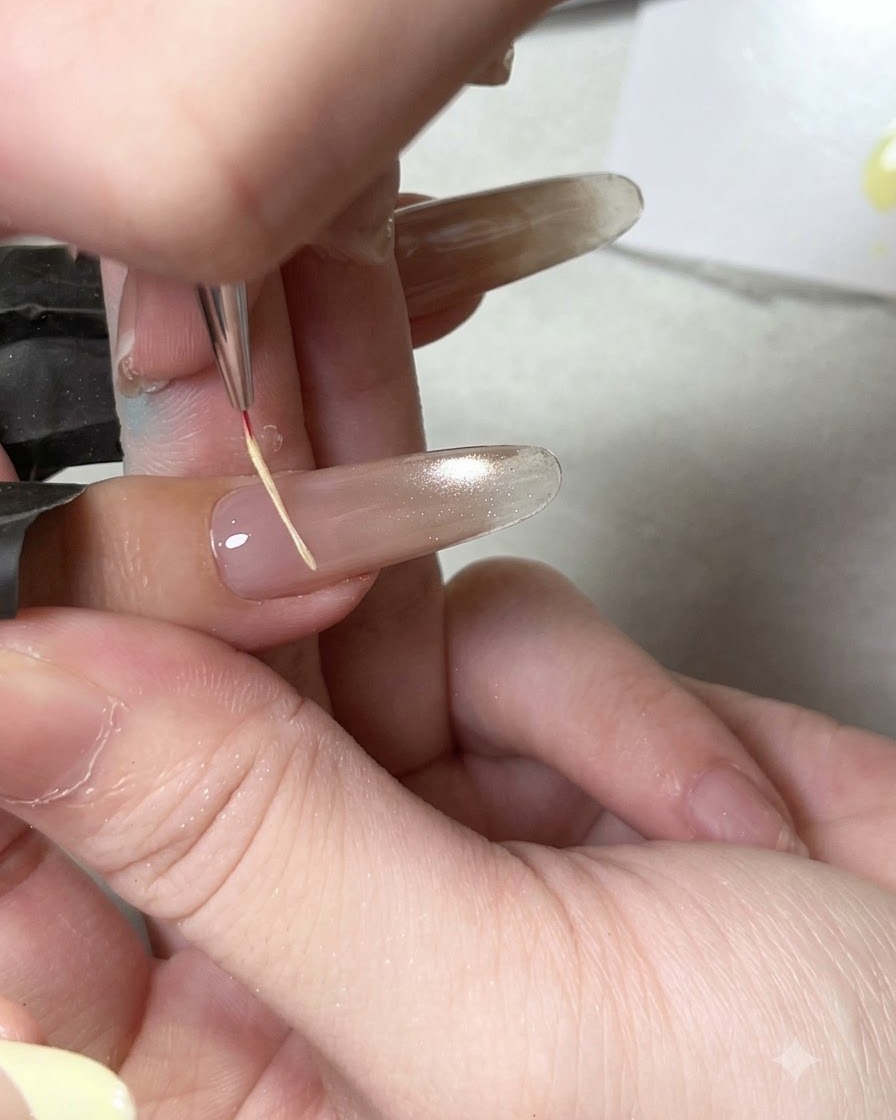 Un pinceau de détail fin appliquant un top coat brillant sur une base dongle cat eye catalysée.