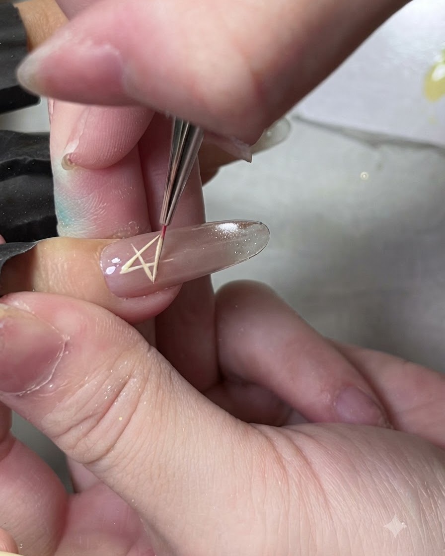 Un pinceau liner fin dessinant le contour dune forme détoile sur un ongle à laide de gel jaune.