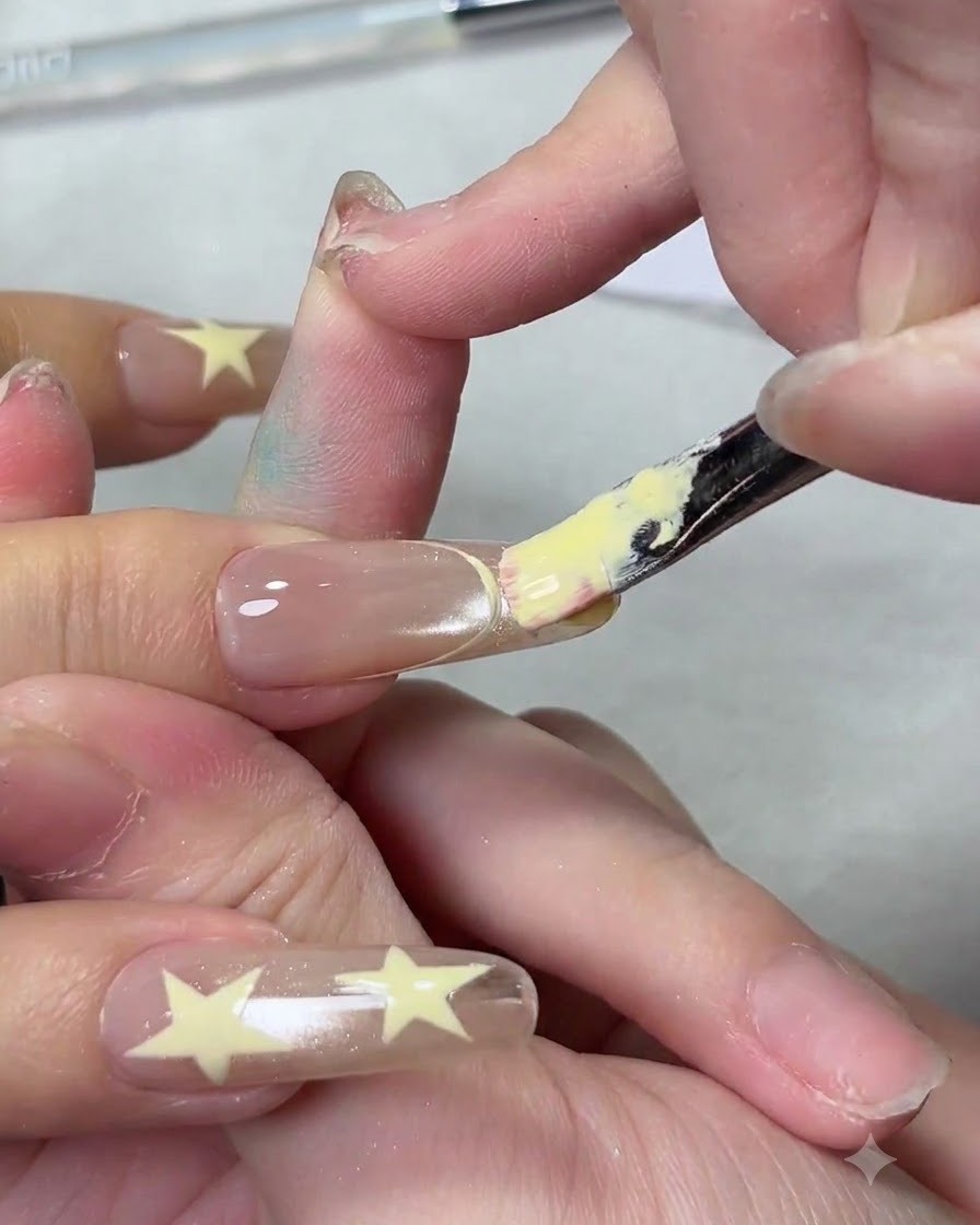Un pinceau à ongles plat appliquant un vernis gel jaune crémeux sur le bout dun ongle pour créer une French manucure.