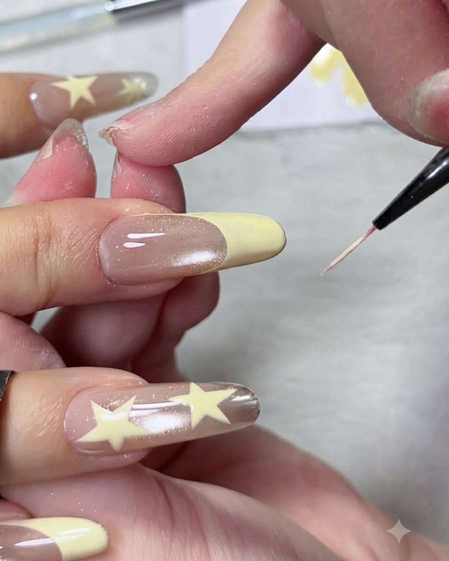 Gros plan dun pinceau liner fin façonnant et aiguisant la ligne du sourire dune pointe de French manucure jaune pastel sur un long ongle en amande.