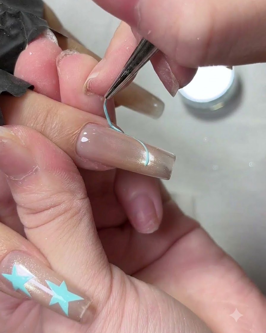 Un pinceau liner fin traçant le contour dune ligne de sourire French tip bleu clair sur un ongle manucuré.