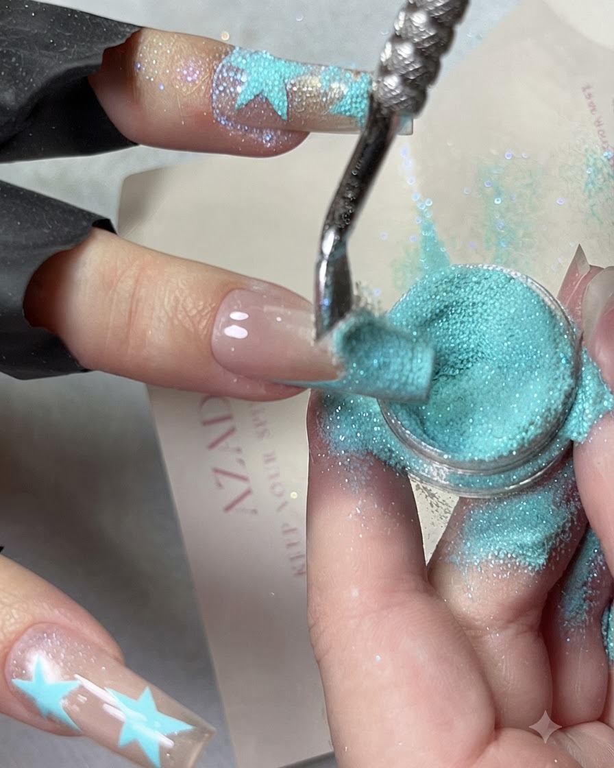 Image de gros plan montrant de la poudre de diamant concassée bleu bébé en train dêtre cascadée sur un design de French tip bleue.