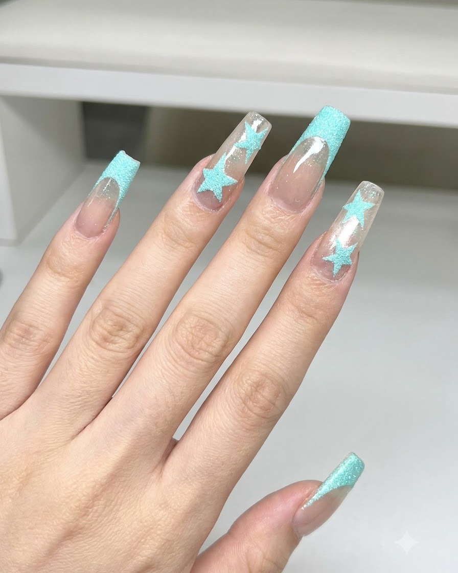 Une brosse à épousseter nettoyant la poudre de paillettes bleues sur de longs ongles carrés présentant un art détoile bleue et des French tips.