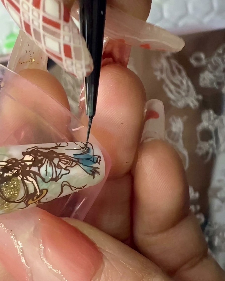 Tampon transparent pressé sur un faux ongle pour y transférer une figure détaillée marron.