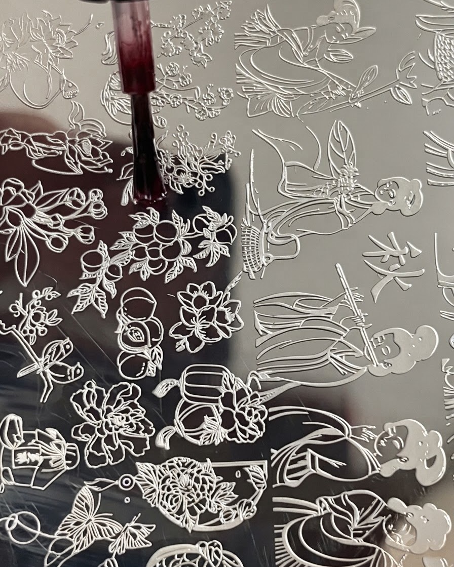 Un pinceau appliquant du liquide blooming sur une gravure florale sur une plaque destampage métallique.