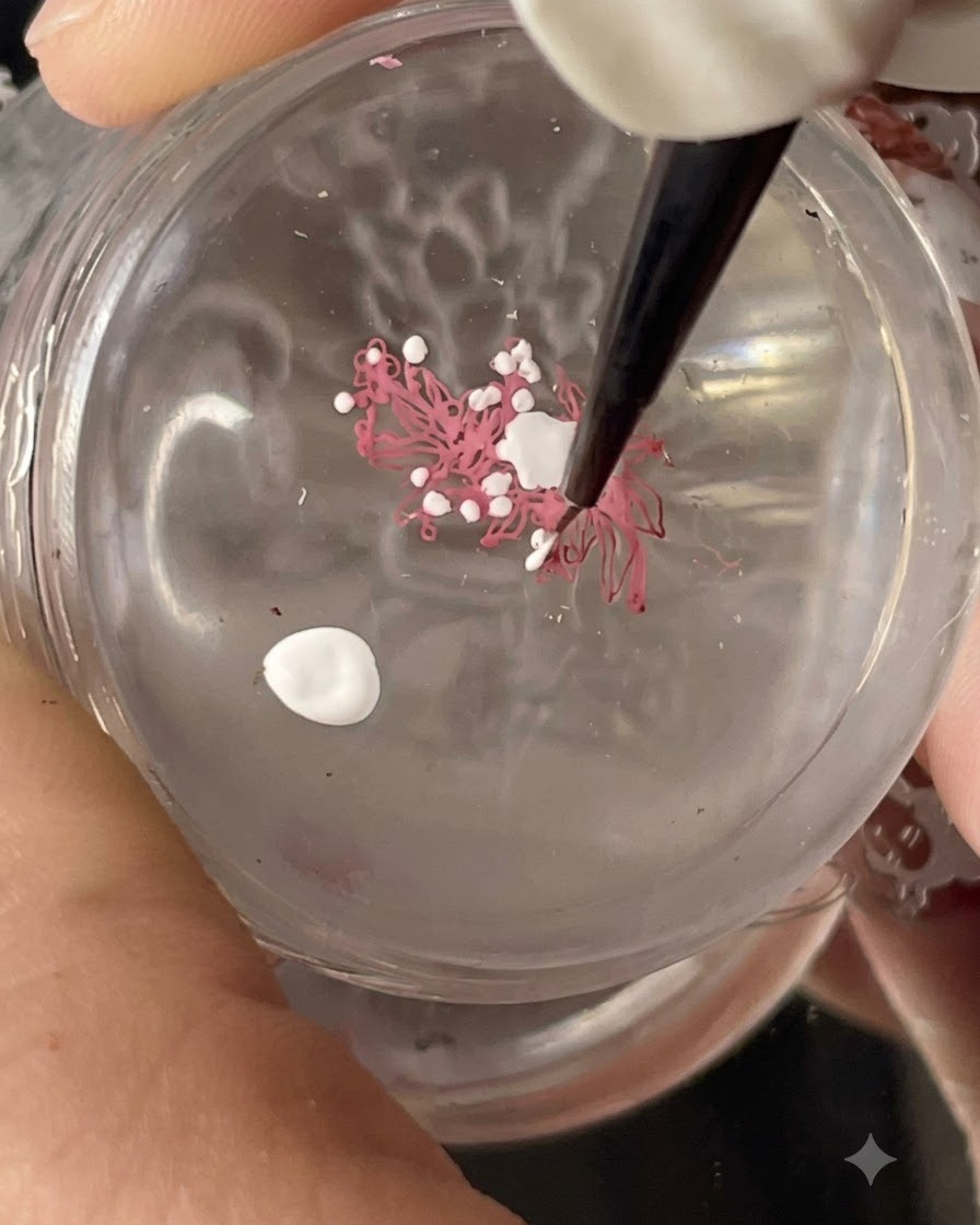 Un tampon en silicone transparent tenant un design destampage floral transféré tandis que des points blancs sont ajoutés avec un pinceau fin.