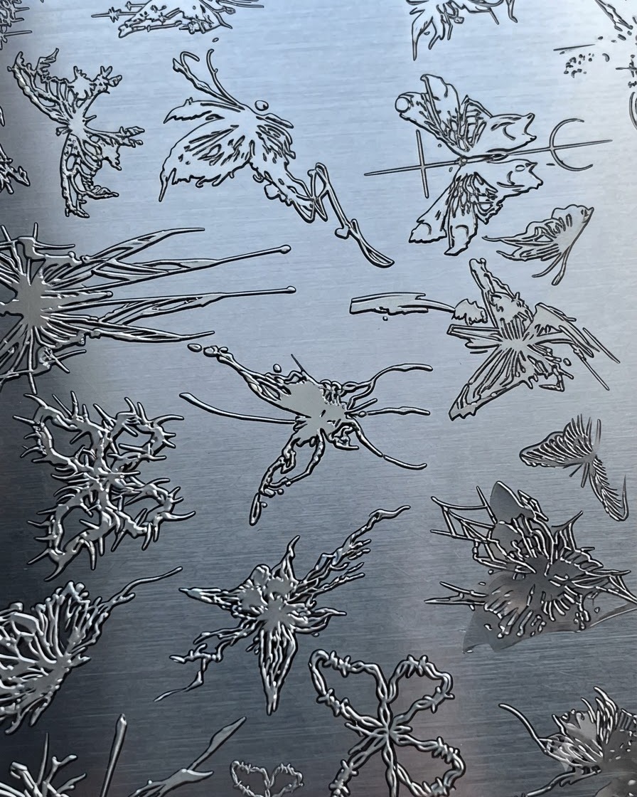 Une plaque destampage métallique présentant divers motifs complexes de papillons et abstraits.