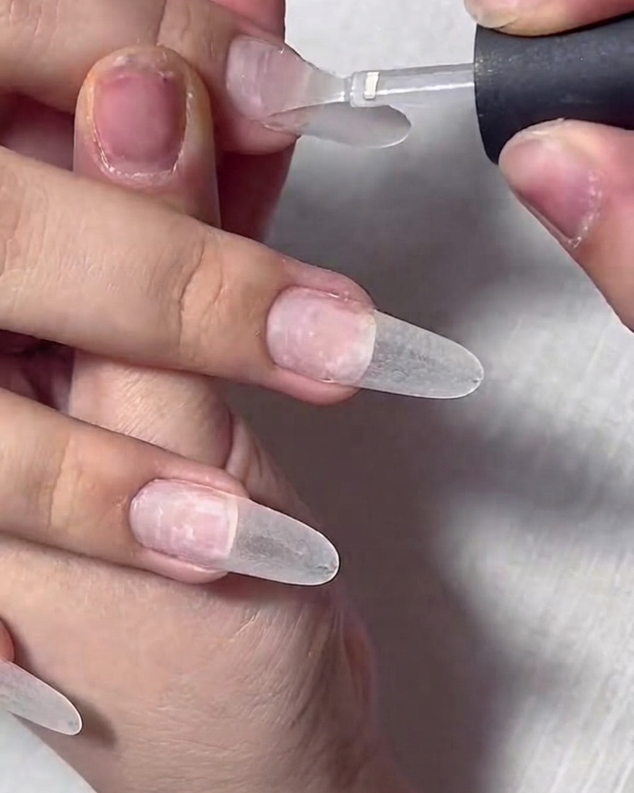 Gros plan dun pinceau appliquant du gel de base transparent sur un ongle naturel préparé.
