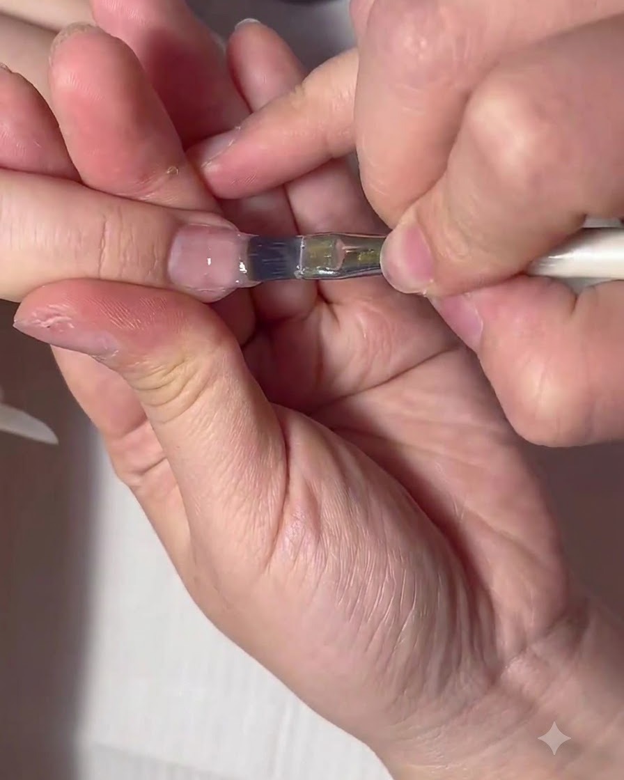 Un pinceau plat pour gel manipulant une grosse boule de gel de construction transparent sur la surface de longle.