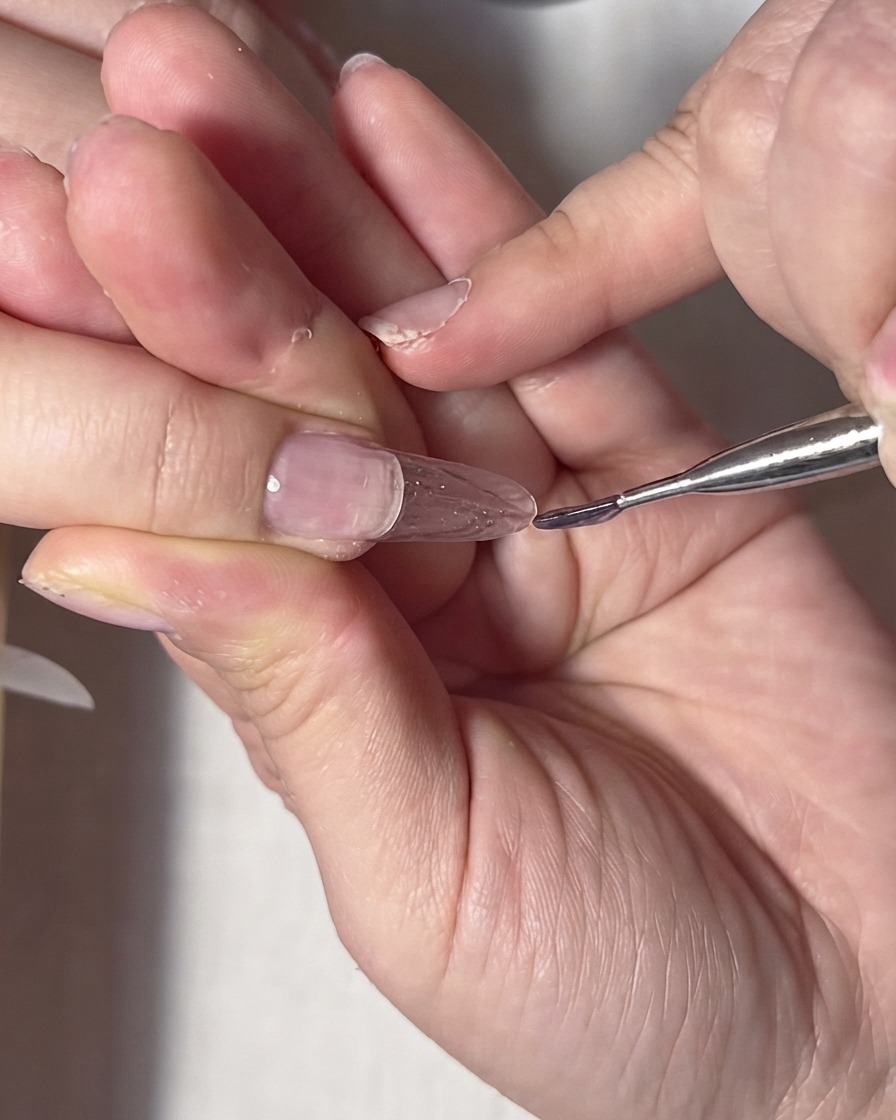 Un pinceau liner fin ajustant le gel transparent près de la ligne des cuticules et des bords latéraux de longle.