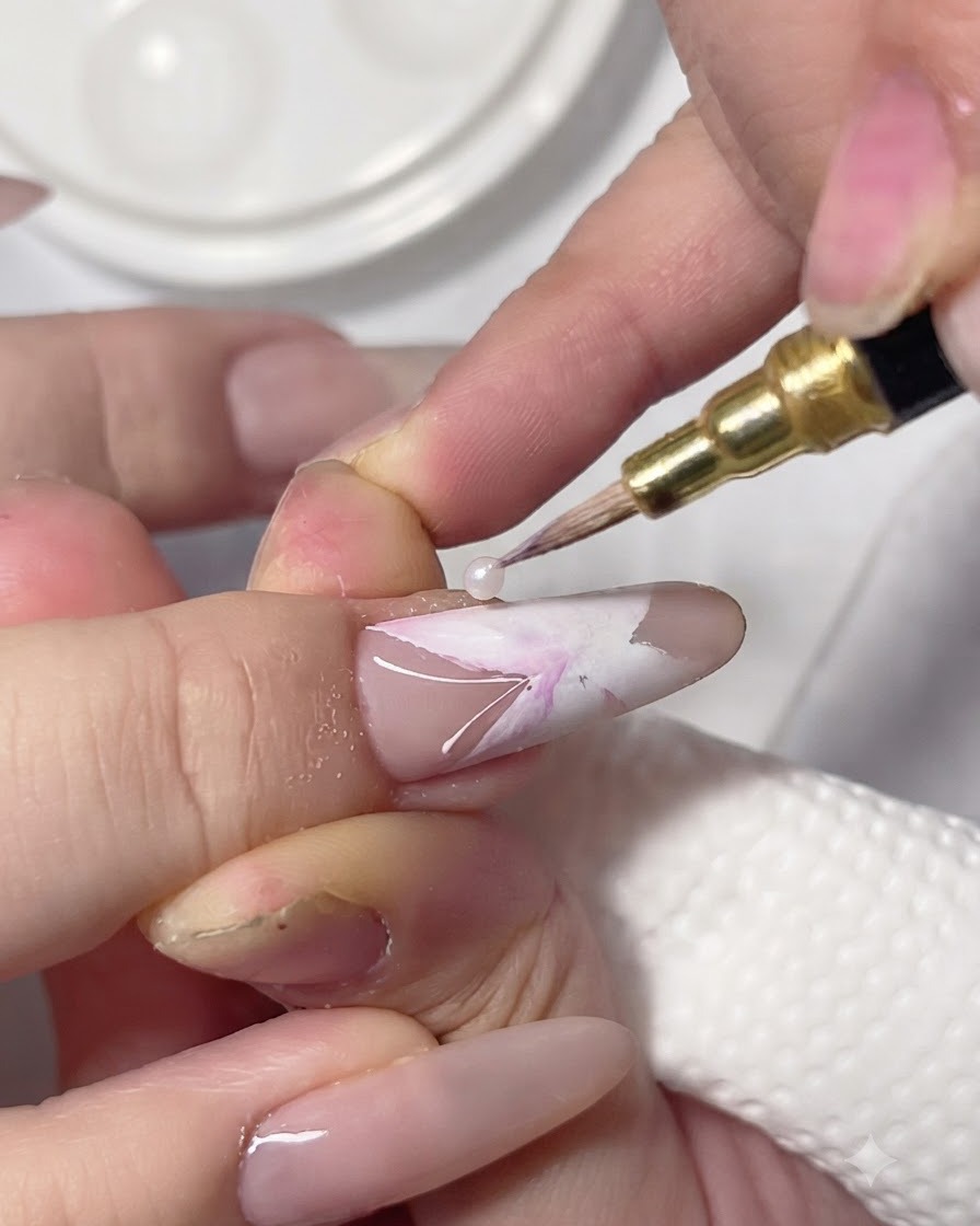 Un pinceau de détail déposant des pigments rose et violet dans les sections blanches humides dun nail art papillon sur ongle.