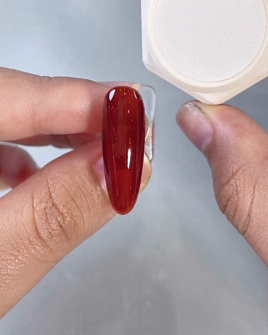 Un gel liquide rouge foncé recouvrant un seul ongle artificiel allongé vu de près.