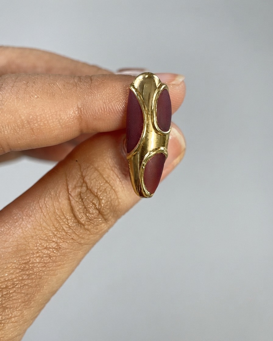Un pinceau à poussière duveteux balayant la surface dun ongle texturé bordeaux et doré.