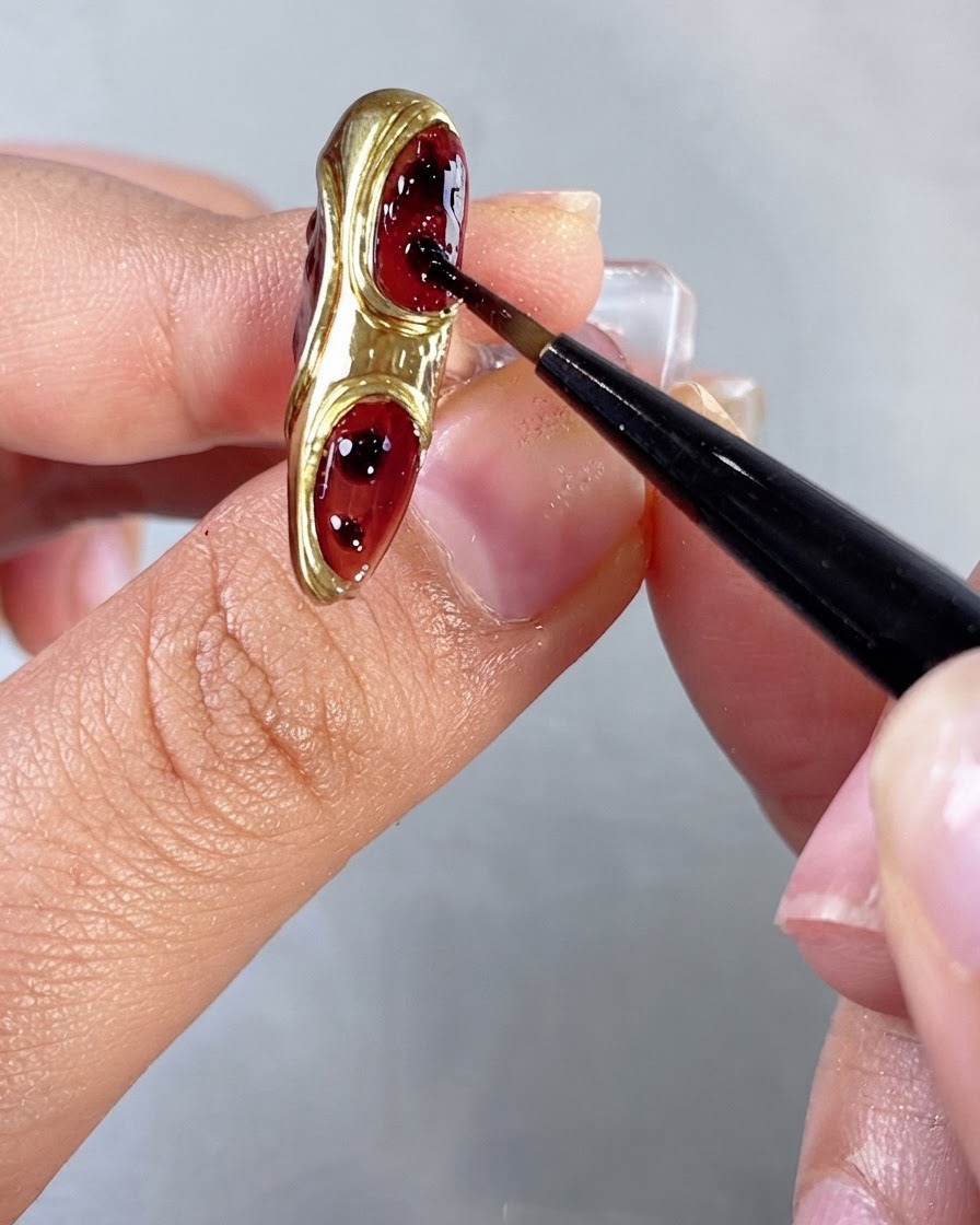 Un pinceau étirant et estompant de petits points de gel rouge à lintérieur des espaces en creux des ongles.
