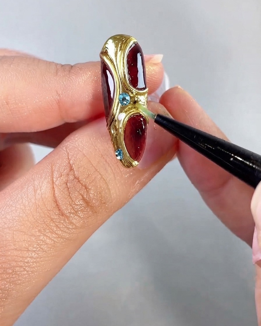 Une pince à épiler positionnant de petits strass bleus le long des sections texturées dorées et incurvées du nail art.