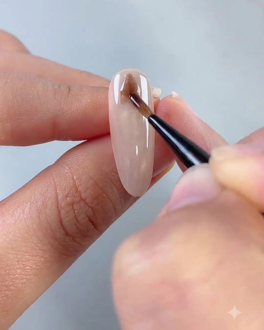 Un pinceau liner fin dessinant une forme de losange marron foncé près de la base dun ongle cat eye.