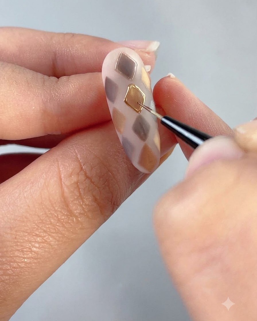 Un pinceau fin dessinant un contour en gel transparent autour dune forme de diamant doré sur un ongle décoré.