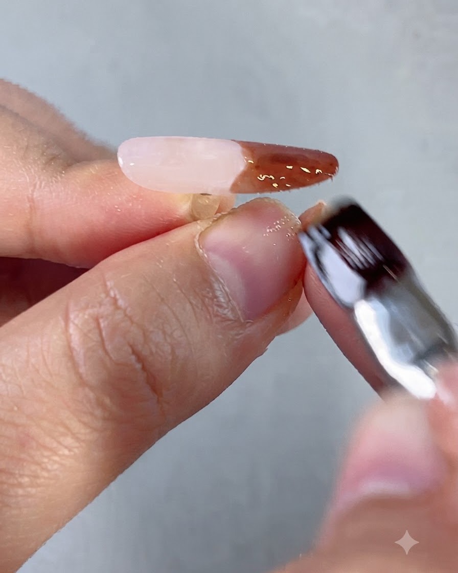 Un pinceau liner fin positionnant de minuscules billes dacier dorées à côté de strass bleus sur un design dongle orné.