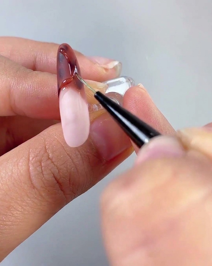 Un pinceau appliquant une couche de top coat sur une base dongle rose laiteux catalysée dans le cadre dun tutoriel multi-ongles.