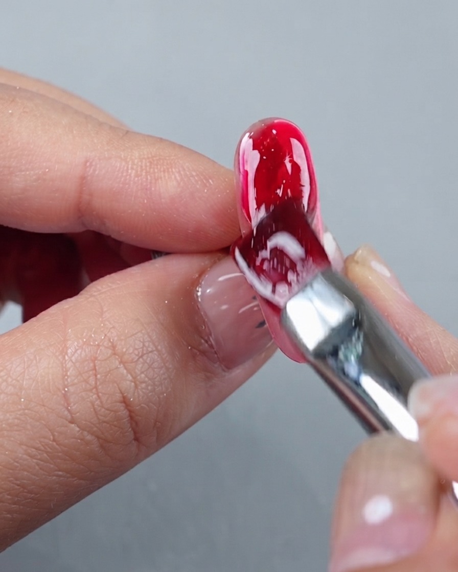 Un pinceau à ongles appliquant une couche épaisse et brillante de gel de construction rouge sur une extension dongle manucurée.