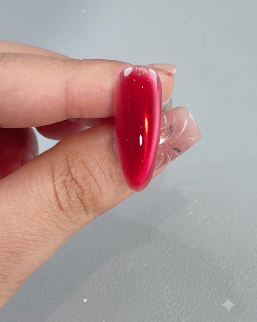 Un pinceau appliquant une couche de top coat brillant sur un ongle crystal red cat eye catalysé.